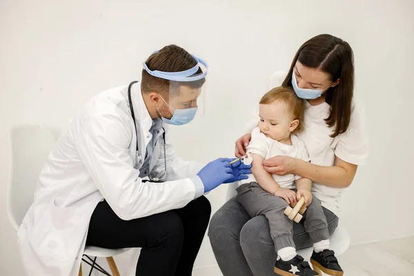 Male doctor doing a vaccination to a little boy who sitting on mothers lap — Zdjęcie stockowe