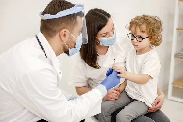 Чоловік-лікар робить вакцинацію маленькому хлопчику, який сидить на матерях — стокове фото