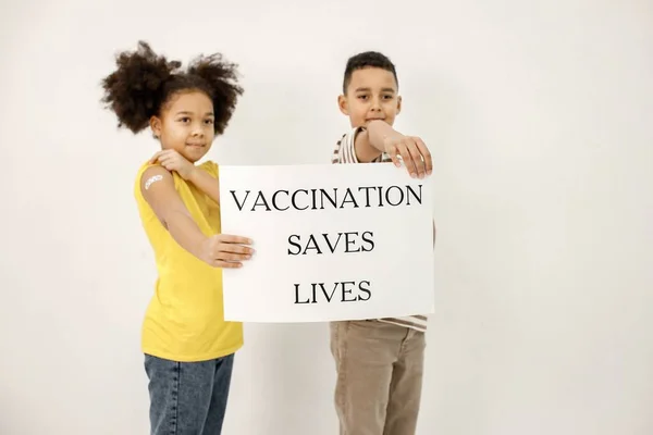 Two multiracial kids holding a poster that vaccination saved lives — ストック写真