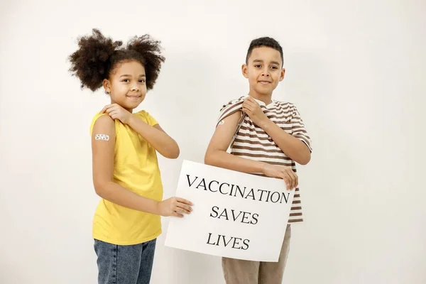 Zwei multiethnische Kinder mit einem Poster, dass Impfungen Leben retteten — Stockfoto
