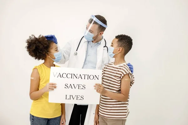 Two multiracial kids with doctor holding a poster that vaccination saved lives — стоковое фото