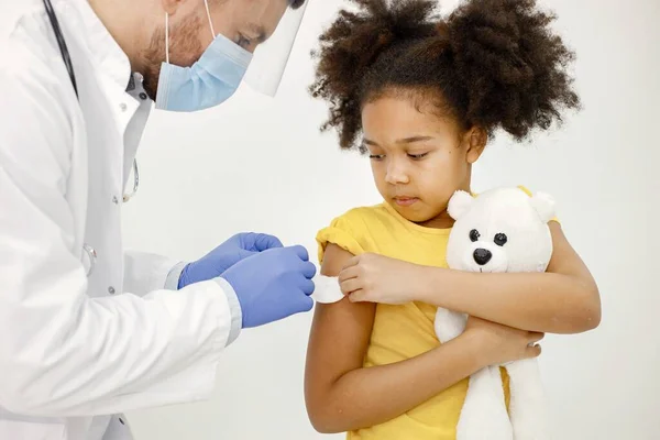 Male doctor stick a band-aid on a girls shoulder after a vaccination — Zdjęcie stockowe