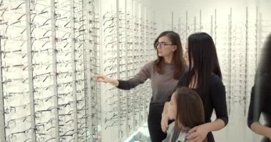 Parents with cute daughter try on glasses in a modern optics store