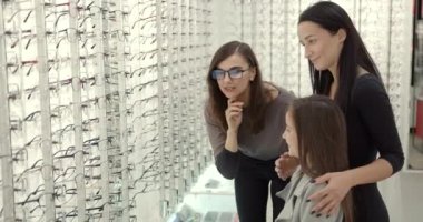 Parents with cute daughter try on glasses in a modern optics store