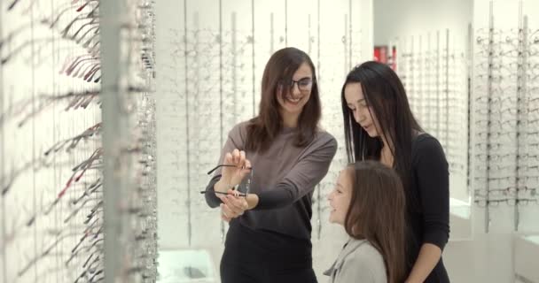 Parents with cute daughter try on glasses in a modern optics store — Video