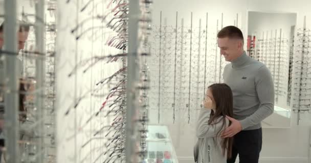 ผู้หญิงวัยรุ่นที่มีพ่อใกล้หน้าต่างร้านในร้านแว่นตาสมัยใหม่ — วีดีโอสต็อก