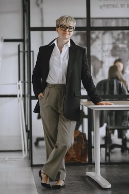 Woman with glasses standing in the office at the table.