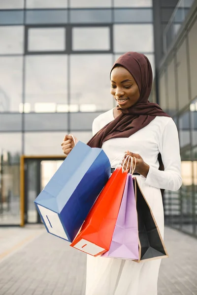 Arabic woman wearing hijab standing with shopping bags near mall