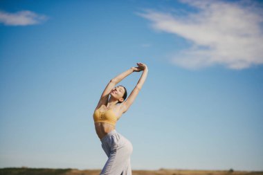 Gökyüzü arka planında eğitim alan güzel bir kız. Sarı bluzlu kadın. Bayan yoga yapıyor.