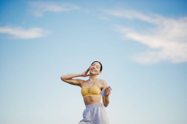 Gökyüzü arka planında eğitim alan güzel bir kız. Sarı bluzlu kadın. Bayan yoga yapıyor. Cep telefonu olan kız.