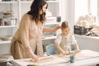 Kadın ve kız kil yoğuruyor. Aile, çömlekçilik atölyesindeki masada sanat ürünü yapıyor. Anne ve kızı..