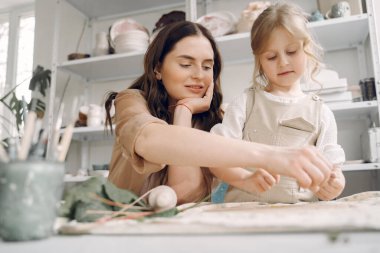 Kadın ve kız kil yoğuruyor. Aile, çömlekçilik atölyesindeki masada sanat ürünü yapıyor. Anne ve kızı..