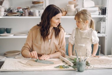 Kadın ve kız kil yoğuruyor. Aile, çömlekçilik atölyesindeki masada sanat ürünü yapıyor. Anne ve kızı..