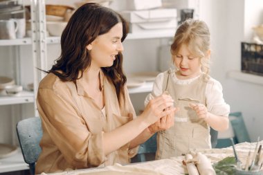 Kadın ve kız kil yoğuruyor. Aile, çömlekçilik atölyesindeki masada sanat ürünü yapıyor. Anne ve kızı..