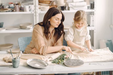 Kadın ve kız kil yoğuruyor. Aile, çömlekçilik atölyesindeki masada sanat ürünü yapıyor. Anne ve kızı..
