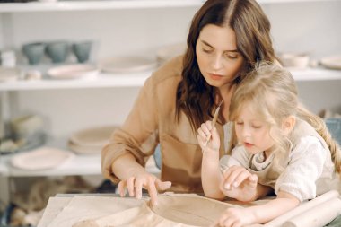 Kadın ve kız kil yoğuruyor. Aile, çömlekçilik atölyesindeki masada sanat ürünü yapıyor. Anne ve kızı..
