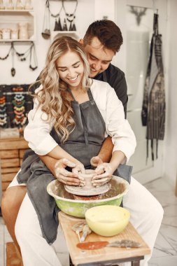 Ortak yaratıcı çalışma. Günlük giysiler ve önlükler içinde genç ve güzel bir çift. İnsanlar kilden bir stüdyoda çömlek çarkında kase yapıyorlar..