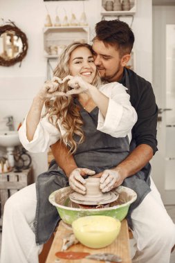 Ortak yaratıcı çalışma. Günlük giysiler ve önlükler içinde genç ve güzel bir çift. İnsanlar kilden bir stüdyoda çömlek çarkında kase yapıyorlar..