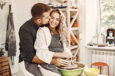 Ortak yaratıcı çalışma. Günlük giysiler ve önlükler içinde genç ve güzel bir çift. İnsanlar kilden bir stüdyoda çömlek çarkında kase yapıyorlar..