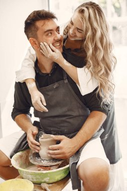 Ortak yaratıcı çalışma. Günlük giysiler ve önlükler içinde genç ve güzel bir çift. İnsanlar kilden bir stüdyoda çömlek çarkında kase yapıyorlar..