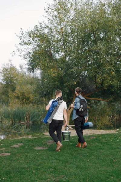 Friends is ready to fishing. Men holding a fishing equipment. One man wearing rose t-shirt and other blue shirt.