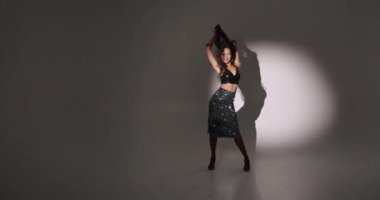 Çekici, kıvırcık saçlı, stil sahibi bir kadının eğlenmesi, dans etmesi, Noel partisinin tadını çıkarması, ellerini kaldırıp gülümsemesi, kendi vücudunun tadını çıkarması, ritme ayak uydurması, karanlık arka plana geçmesi..