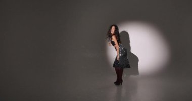 Çekici, kıvırcık saçlı, stil sahibi bir kadının eğlenmesi, dans etmesi, Noel partisinin tadını çıkarması, ellerini kaldırıp gülümsemesi, kendi vücudunun tadını çıkarması, ritme ayak uydurması, karanlık arka plana geçmesi..