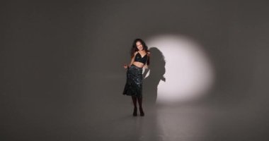 Çekici, kıvırcık saçlı, stil sahibi bir kadının eğlenmesi, dans etmesi, Noel partisinin tadını çıkarması, ellerini kaldırıp gülümsemesi, kendi vücudunun tadını çıkarması, ritme ayak uydurması, karanlık arka plana geçmesi..