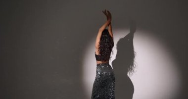 Çekici, kıvırcık saçlı, stil sahibi bir kadının eğlenmesi, dans etmesi, Noel partisinin tadını çıkarması, ellerini kaldırıp gülümsemesi, kendi vücudunun tadını çıkarması, ritme ayak uydurması, karanlık arka plana geçmesi..