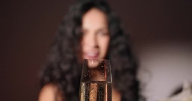 Çekici Latin kadın gülümsüyor ve elinde bir kadeh şampanya ya da stüdyo arka planında şarap tutuyor. Parti havası.