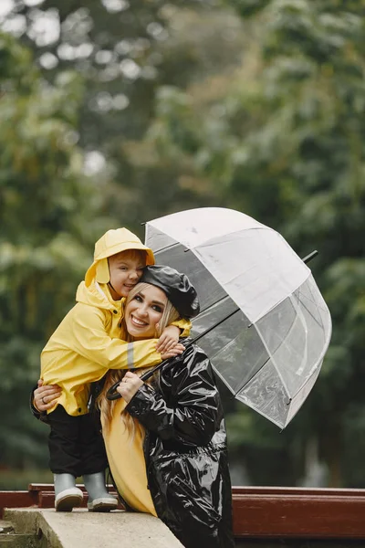 Family in a rainy park. Kids in a raincoats. Mother with child. Woman in a black coat.