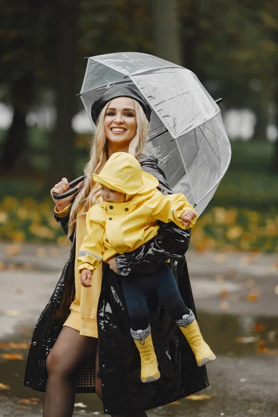 Family in a rainy park. Kids in a raincoats. Mother with child. Woman in a black coat.