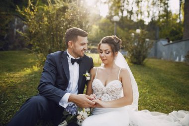 Genç ve güzel bir gelin ve kocası bir buket çiçekle bir yaz parkında dikiliyor.