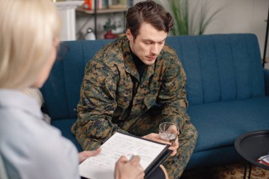 Terapi sırasında koltukta oturan asker ve psikiyatristin kesilmiş fotoğrafı. Askeri üniforma giyen adam. Psikiyatristle konuşan erkek savaşçı..