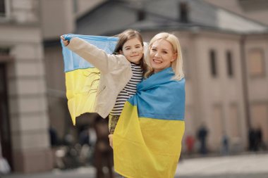 Genç anne ve kızı eski kasabanın caddesinde dikiliyorlar. Kız ve kadın ellerinde Ukrayna 'nın büyük bayrakları, mavi ve sarı renklerde. Kadın ve kız Ukrayna 'yı savaşa karşı destekliyor.