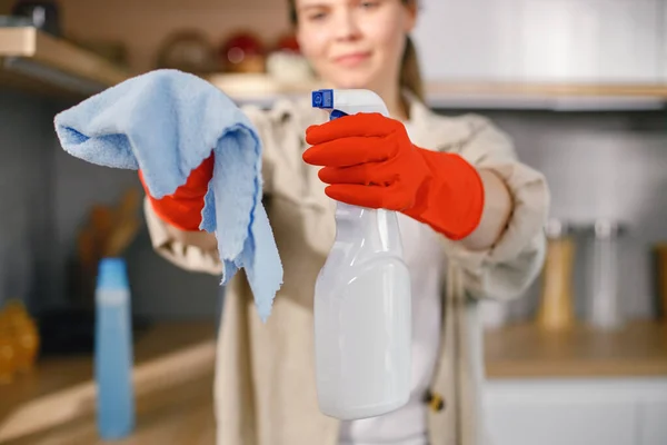 Cropped photo of woman cleaning in a kitchen and wearing red gloves. Focus on a spraying detergent and a rug. Cleaning concept.