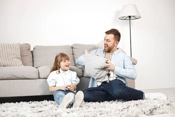 Loving father playing with his daughter with Down syndrome at home together. Man and girl sitting on a floor near sofa. Bearded man wearing blue shirt and girl white shirt.