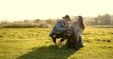 Şapkalı bir adam ve doğada köpekle oynayan gözlüklü bir kadın. Açık hava eğlencesi.