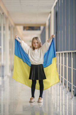 Ukrayna bayrağı taşıyan küçük bir kız fotoğraf için poz veriyor. Cam duvarın önünde duran genç ve güzel bir kız. Ukrayna 'yı destekleyen kız.