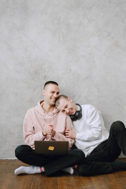 Genç eşcinsel çift yerde dizüstü bilgisayar kullanıyor, kulaklık takıyor birlikte müzik dinliyor, sarılıyor ya da kucaklıyor..