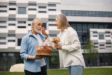 Yazın çimlerin üzerinde duran Kafkasyalı yaşlı çift. Saman sepeti tutan adam ve kadın elma. Beyaz tişörtlü kadın ve mavi erkek..
