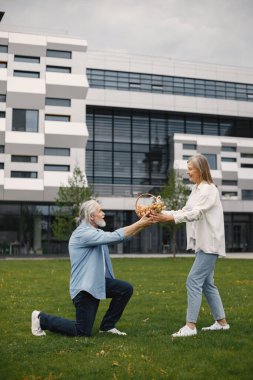Yazın çimlerin üzerinde duran Kafkasyalı yaşlı çift. Adam dizinin üstünde duruyor, saman sepetini tutuyor ve karısına veriyor. Beyaz tişörtlü kadın ve mavi erkek..