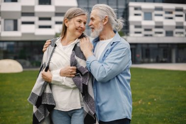 Yazın çimlerin üzerinde duran Kafkasyalı yaşlı çift. Erkek ve kadın sarılıyor. Beyaz gömlekli ve ekose battaniyeli bir kadın..