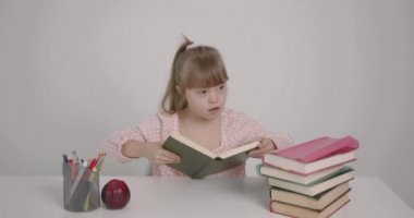 Akıl hastası küçük bir kız masada oturuyor. O bir kitabı inceliyor. Engelli çocuk.