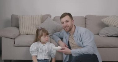 Avrupalı bir ebeveyn ve özel ihtiyaçları olan bir kız koltukta yerde oturuyor. Film izlemek, kaynaşmak. .