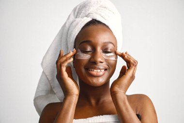 Beyaz arka planda yüzü yamalı siyah genç bir kadın. Kız saçını havluya sarmış. Siyahi kadın, vücut tedavisinden sonra.