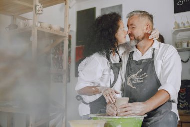 Mutual creative work. Adult elegant couple in casual clothes and aprons. People creating a bowl on a pottery wheel in a clay studio.