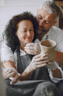 Mutual creative work. Adult elegant couple in casual clothes and aprons. People creating a bowl on a pottery wheel in a clay studio.