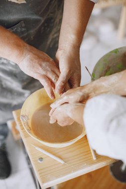 Ortak yaratıcı çalışma. Günlük giysiler ve önlükler içinde yetişkin, zarif bir çift. İnsanlar kilden bir stüdyoda çömlek çarkında kase yapıyorlar..