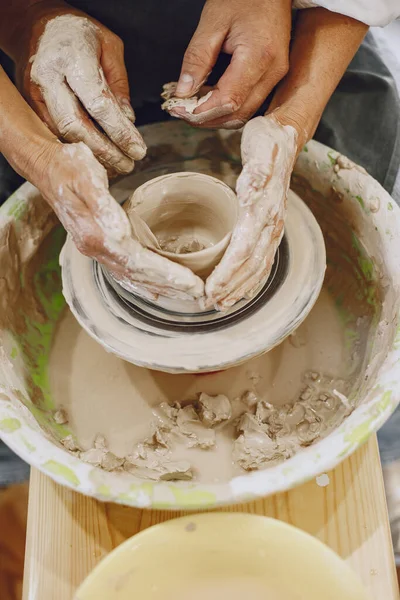 Mutual creative work. Adult elegant couple in casual clothes and aprons. People creating a bowl on a pottery wheel in a clay studio.